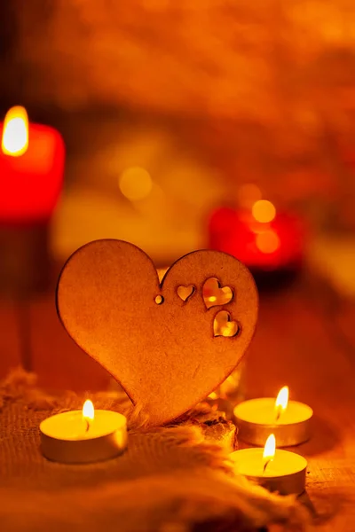 Wooden heart and candles on burlap and wooden boards. St Valentine\'s day greeting card with candle and heart on a blurred background. Love story concept. Copy space