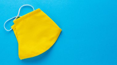 Sarı pamuktan yapılmış yeniden kullanılabilir yüz maskesi. Yüz koruyucu maske. Mavi arka planda sarı koruyucu maske. Pop sanat tarzı. Üst Manzara. Boşluğu kopyala