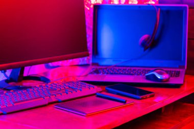 Dijital tasarımcı işyeri. Uzaktan kumanda. Neon ışığı altında serbest çalışan bir işyeri. Bilgisayar, dizüstü bilgisayar, grafik tableti ve akıllı telefon masada.