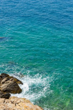 Ege Denizi 'nin turkuaz sularının dikey görüntüsü. Turkuaz suyun önünde vahşi kayalıklar. Deniz kenarında yaz tatili