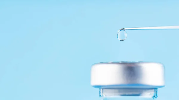 Vaccine drop on syringe needle. Vaccination concept, disease prevention. Needle with a drop of vaccine on a blue background. Coronavirus vaccine development