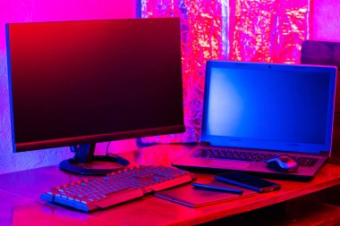 Dijital tasarımcı işyeri. Uzaktan kumanda. Neon ışığı altında serbest çalışan bir işyeri. Bilgisayar, dizüstü bilgisayar, grafik tableti ve akıllı telefon masada.