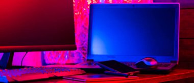 Dijital tasarımcı işyeri. Uzaktan kumanda. Neon ışığı altında serbest çalışan bir işyeri. Bilgisayar, dizüstü bilgisayar, grafik tableti ve akıllı telefon masada.