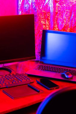 Dijital tasarımcı işyeri. Uzaktan kumanda. Neon ışığı altında serbest çalışan bir işyeri. Bilgisayar, dizüstü bilgisayar, grafik tableti ve akıllı telefon masada.