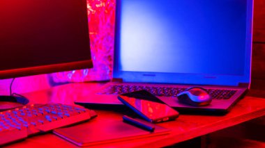 Dijital tasarımcı işyeri. Uzaktan kumanda. Neon ışığı altında serbest çalışan bir işyeri. Bilgisayar, dizüstü bilgisayar, grafik tableti ve akıllı telefon masada.