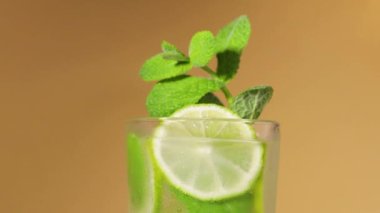 Mojito. Limon dilimleri ve nane yapraklarıyla dönen bir mojito bardağının yakın çekimi.