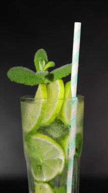 Mojito kokteyli. Limon dilimleri ve nane yapraklarıyla dönen bir mojito bardağının yakın çekimi. Dikey video