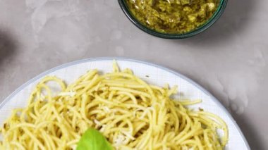 Pesto soslu spagetti, peynir ve taze fesleğen. Mutfak masasında soslu İtalyan makarnası. Üst görünüm