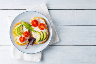 Krem peynirli ve vişneli domatesli avokado tostu. Beyaz tahtalarda avokado ve roka ile iki tost. Uzayı kopyala Üst görünüm