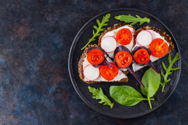 Krem peynirli sağlıklı tost, vişneli domates ve siyah tabakta ıspanak. Koyu arkaplanda krem peynirli, taze otlu Uzayı kopyala Üst görünüm