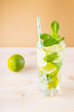 Büyük bardakta mojito kokteyli. Altın arka planda yaz kokteyli, limon ve tahta sıkacağı. Limonlu, naneli ve buzlu içecek.