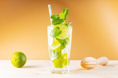 Büyük bardakta mojito kokteyli. Altın arka planda yaz kokteyli, limon ve tahta sıkacağı. Limonlu, naneli ve buzlu içecek.