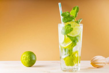 Büyük bardakta mojito kokteyli. Altın arka planda yaz kokteyli, limon ve tahta sıkacağı. Limonlu, naneli ve buzlu içecek.