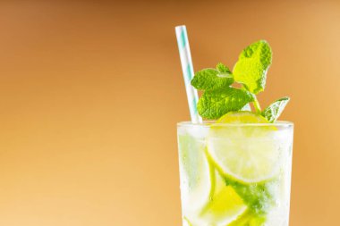 Büyük bardakta mojito kokteyli. Altın arka planda yaz kokteyli, limon ve tahta sıkacağı. Limonlu, naneli ve buzlu içecek.