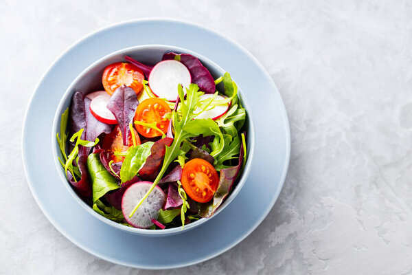 Healthy vegetable salad with cherry tomatoes, radish and mix salad. Vegan salad with mix of greens on gray background. Paleo diet concept. Copy space. Top view