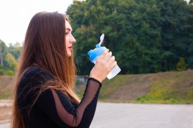Güzel genç kız egzersizden sonra parkta su içer. Koşudan sonra parkta su içen sportif kadın portresi. Antrenmandan sonra bayan sporcu. Boşluğu kopyala
