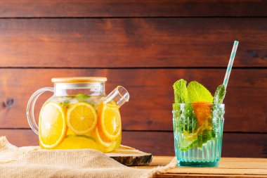 Şeffaf çaydanlıkta limonlu buzlu çay. Limonata, limon, portakal ve nane yaprakları ahşap tahtalarda. Boşluğu kopyala