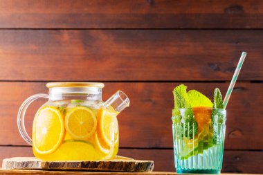Şeffaf çaydanlıkta limonlu buzlu çay. Limonata, limon, portakal ve nane yaprakları ahşap tahtalarda. Boşluğu kopyala