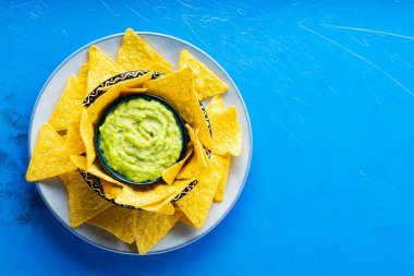 Mavi arka planda tortilla cipsi ve guacamole sosu. Tabakta mısır cipsi ile guacamole. Uzayı kopyala Üst görünüm