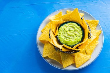 Mavi arka planda tortilla cipsi ve guacamole sosu. Tabakta mısır cipsi ile guacamole. Uzayı kopyala Üst görünüm