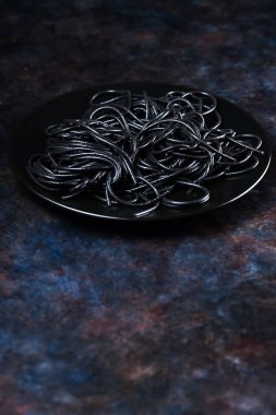Siyah tabakta siyah makarna. Siyah spagetti mürekkep balığı mürekkebi ve koyu bir arka plan. Kaynamış siyah spagetti. Uzayı kopyala Minimalizm