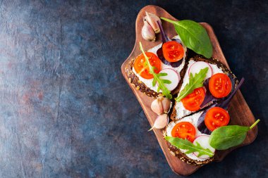 Krem peynirli, kirazlı domatesli ve kesme tahtasında sarımsak. Krem peynirli ve taze otlu İtalyan antipasti bruschetta. Uzayı kopyala Üst görünüm