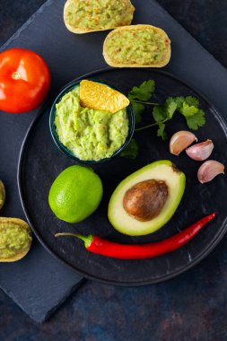 Guacamole sosu, cips ve koyu arkaplanda malzemeler. Meksika soslu avokado, malzemeler ve mısır cipsi. Uzayı kopyala Üst görünüm