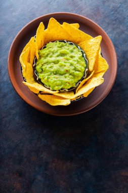 Geleneksel Meksika soslu guacamole ve kil kasesinde tortilla cipsi. Koyu arkaplanda cipsli bir kase guacamole. Uzayı kopyala Üst görünüm