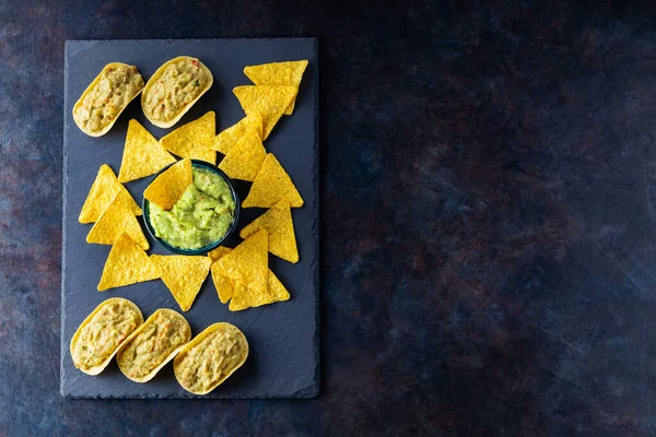 Mexican guacamole sauce with nachos chips on a slate board. Tortilla chips and guacamole on a dark background. Copy space. Top view