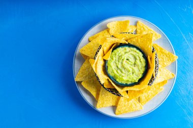 Mavi arka planda tortilla cipsi ve guacamole sosu. Tabakta mısır cipsi ile guacamole. Uzayı kopyala Üst görünüm