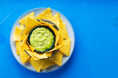 Mavi arka planda tortilla cipsi ve guacamole sosu. Tabakta mısır cipsi ile guacamole. Uzayı kopyala Üst görünüm