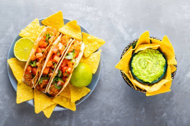 İspanyol Meksikalı yemekleri. Gri arka planda taco ve tortilla cipsi tabağı. Meksika takosu, cips ve guacamole sosu. Uzayı kopyala Üst görünüm