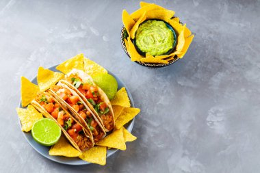 İspanyol Meksikalı yemekleri. Gri arka planda taco ve tortilla cipsi tabağı. Meksika takosu, cips ve guacamole sosu. Uzayı kopyala Üst görünüm