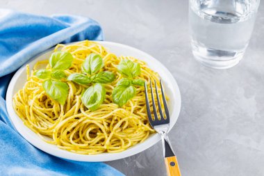 Soslu makarna ve fesleğen yaprağı. Pesto soslu spagetti ve gri arka planda taze fesleğen. İtalyan mutfağı. Yemek tasarımı