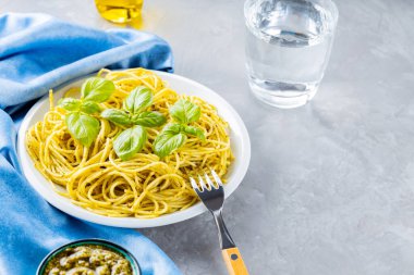 Soslu makarna ve fesleğen yaprağı. Pesto soslu spagetti ve gri arka planda taze fesleğen. İtalyan mutfağı. Yemek tasarımı
