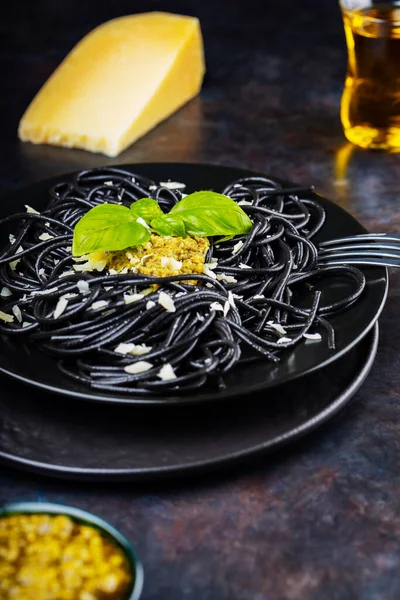 ペストソースと黒スパゲティ バジルとパルメザンチーズ 黒皿の上にイカ墨入りの黒パスタ 伝統的なイタリア料理 — ストック写真