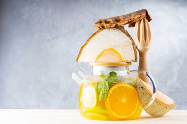 Limonata, limon, portakal ve nane yapraklarından oluşan şeffaf bir çaydanlık. Naneli buzlu çay ve odun parçaları. Yaratıcı bileşim