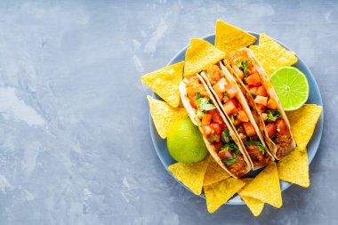 Meksika takoları ve cipsler tabakta. Gri arka planda taco ve tortilla cipsi. İspanyol Meksikalı yemekleri. Uzayı kopyala Düz yatıyordu