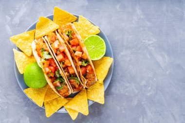 Meksika takoları ve cipsler tabakta. Gri arka planda taco ve tortilla cipsi. İspanyol Meksikalı yemekleri. Uzayı kopyala Düz yatıyordu