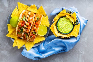 Gri arka planda taco ve tortilla cipsi. Meksika takosu, nacho cipsi ve mavi peçetede guacamole sosu. İspanyol Meksikalı yemekleri. Uzayı kopyala Üst görünüm