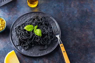 Siyah tabakta mürekkep balığı mürekkebi olan siyah makarna. Pesto soslu siyah spagetti, fesleğen ve parmesan peyniri. Üst Manzara. Boşluğu kopyala
