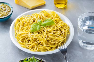 Pesto soslu spagetti ve gri arka planda taze fesleğen. Soslu makarna, fesleğen yaprağı ve malzemeler. İtalyan mutfağı. Yemek tasarımı