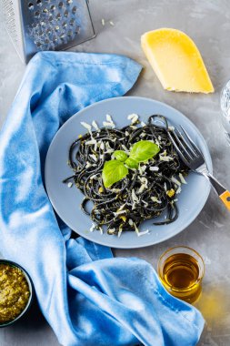 Gri arka planda mürekkep balığı mürekkebi olan siyah spagetti. Parmesan peynirli siyah makarna, fesleğen ve pesto sosu. Rendelenmiş peynirli makarna ve malzemeler. Üst görünüm