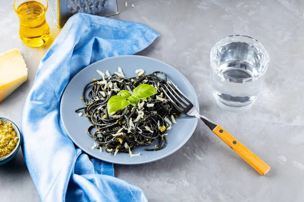 黒スパゲティにイカ墨がグレーの背景に入っています パルメザンチーズと黒パスタ バジルとペストソース チーズと材料をすりおろしたパスタ トップ表示 — ストック写真