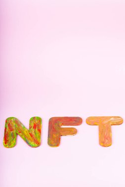 Pembe arka planda NFT yazıları var. Çok renkli harflerden oluşan iadeli olmayan jeton, üst görünüm. Kripto sanat konsepti