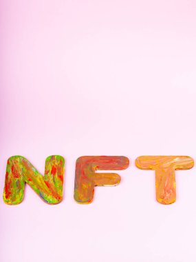 Pembe arka planda NFT yazıları var. Çok renkli harflerden oluşan iadeli olmayan jeton, üst görünüm. Kripto sanat konsepti