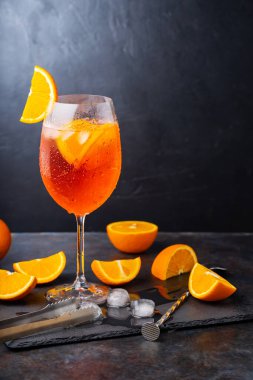 Aperol sprey kokteyli ve bar aksesuarları. İtalyan aperol sprey kokteyli ve koyu arkaplanda dilimlenmiş portakal. Yaz kokteyli aperol spreyini tahtaya serptim.