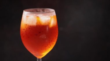 Barmen kokteylin içine bir dilim portakal koyar. Siyah arka planda kokteyl aperol spreyi. Bir bardak yaz portakalı kokteyli. Ağır çekim. Boşluğu kopyala