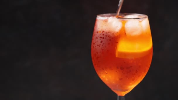 Aperol Spritz Cocktail auf schwarzem Hintergrund. Löffel mixt Getränk. Ein Glas orangefarbener Sommercocktail. Kopierraum. 4k — Stockvideo