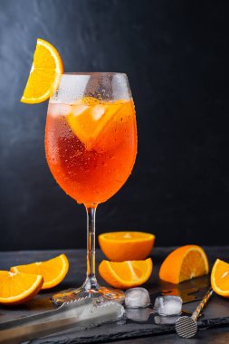 Aperol sprey kokteyli ve bar aksesuarları. İtalyan aperol sprey kokteyli ve koyu arkaplanda dilimlenmiş portakal. Yaz kokteyli aperol spreyini tahtaya serptim.